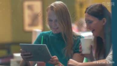 两个女人坐在咖啡馆和笑的东西，<strong>他们</strong>看到的平板电脑镜头是通过咖啡馆